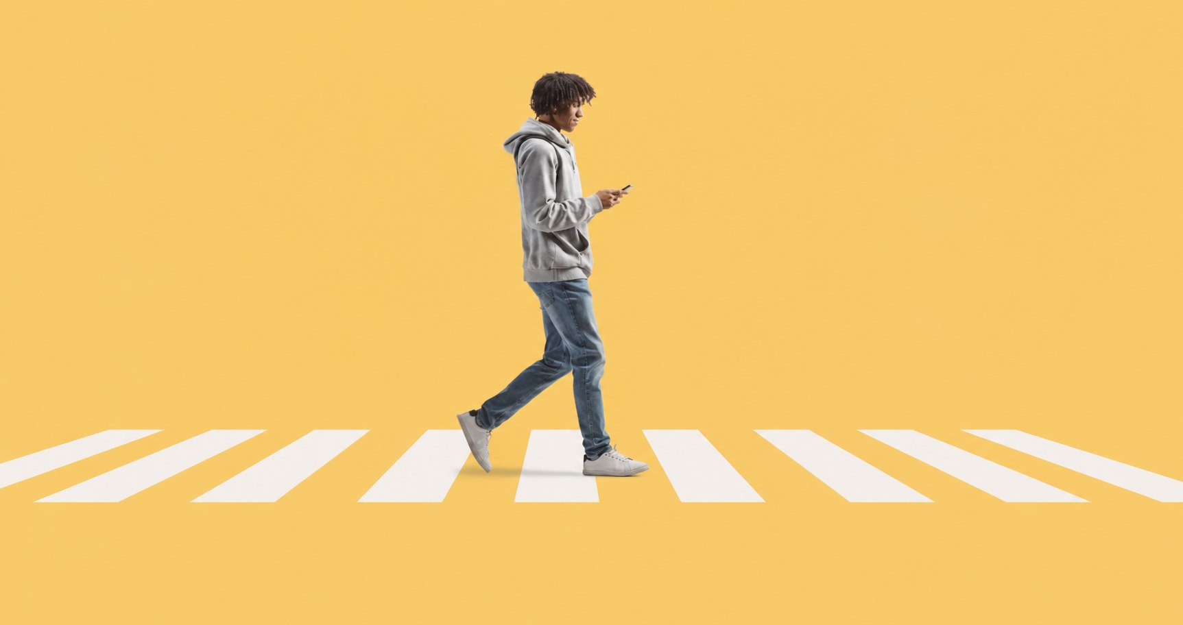 A student walking across a crosswalk while looking at their phone