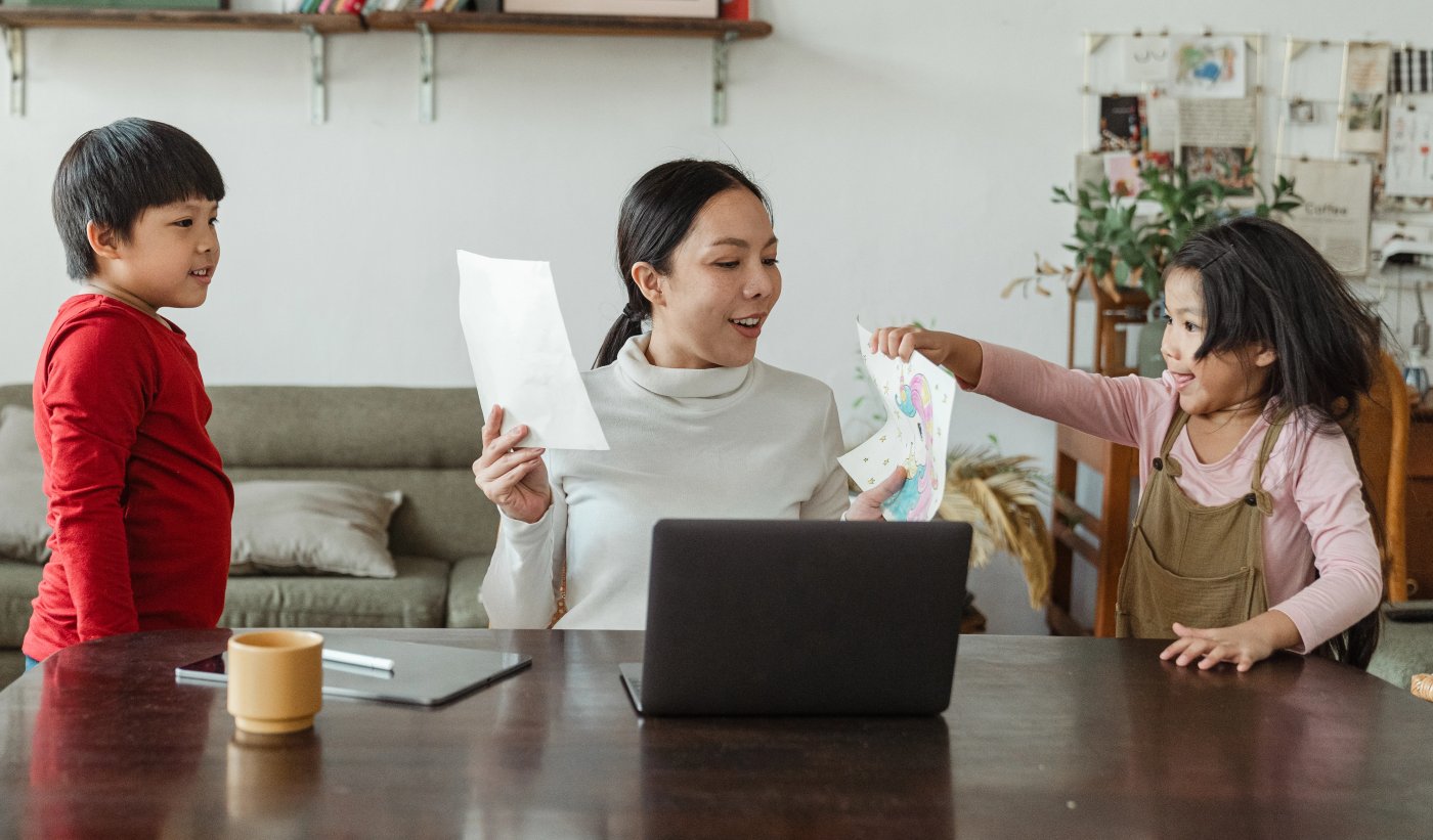 A parent and two children smiling together at a laptop at home