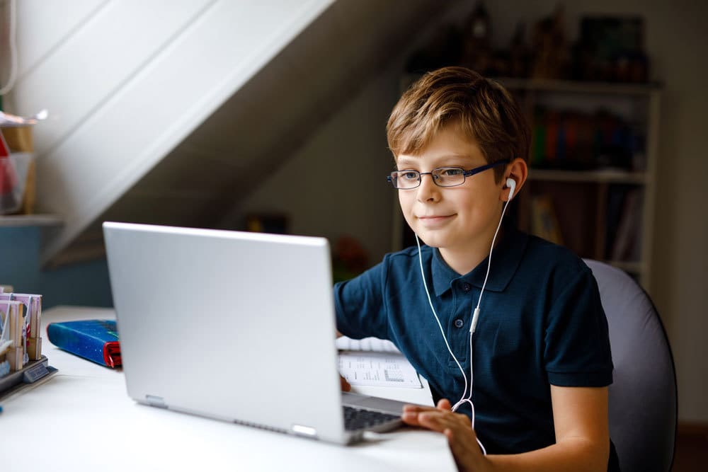 boy wearing earbuds looking at laptop. how to enroll.